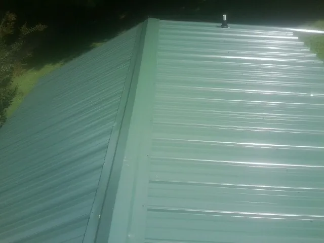 New green metal panels meeting at the ridge of a roof — Flat Roof Repair work by our crew in Hammondsville