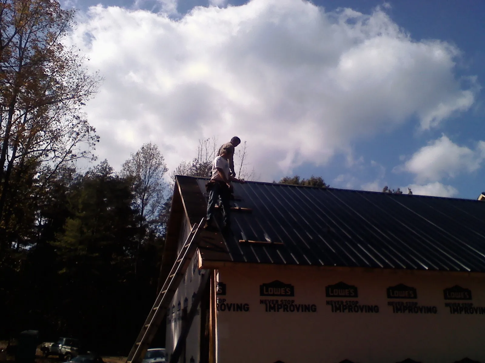 Roofer fastening dark metal panels high against a cloudy sky, from a Roof Inspection job in Hammondsville