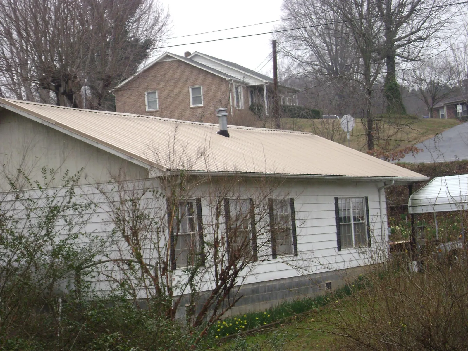 Tan metal roof on a white sided house set into a hillside — Commercial Roofing by Roofing Brothers in Hammondsville